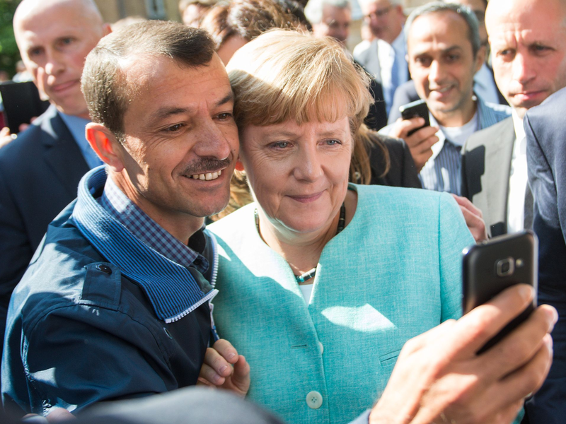 Bald zehn Jahre her: Angela Merkel (CDU) lässt sich nach dem Besuch einer Erstaufnahmeeinrichtung für Asylbewerber in Berlin-Spandau für ein Selfie zusammen mit einem Flüchtling fotografieren. (Archivbild) - Foto: Bernd von Jutrczenka/dpa