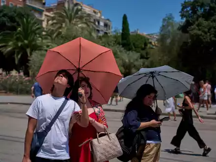 Touristen schützen sich amvor der Kirche Sagrada Familia mit Regenschirmen vor der Sonne.  - Foto: Emilio Morenatti/AP/dpa
