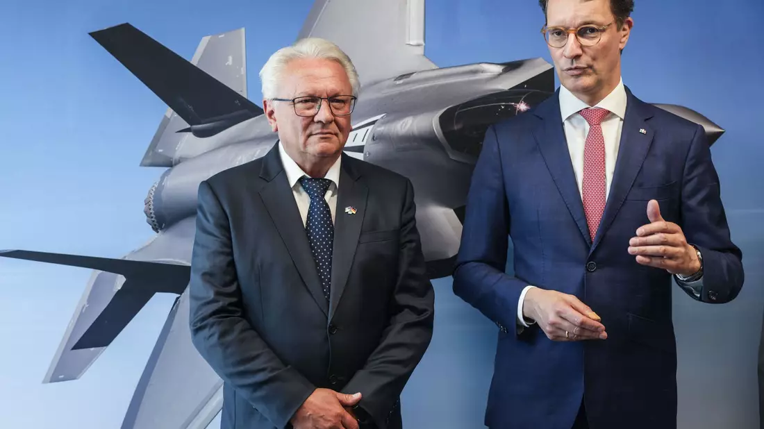 Papperger und Wüst vor einem Bild des F-35-Flugzeugs. Ende nächsten Jahres soll das erste Rumpfmittelteil dieses Tarnkappenbombers in Weeze fertig sein. - Bild: Oliver Berg/dpa