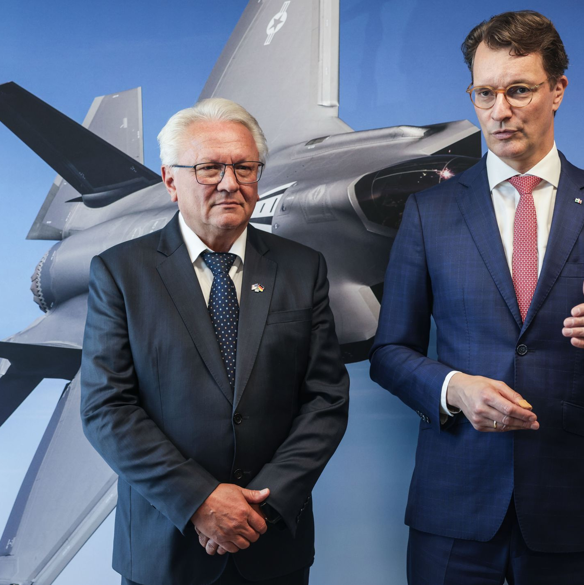 Papperger und Wüst vor einem Bild des F-35-Flugzeugs. Ende nächsten Jahres soll das erste Rumpfmittelteil dieses Tarnkappenbombers in Weeze fertig sein. - Foto: Oliver Berg/dpa