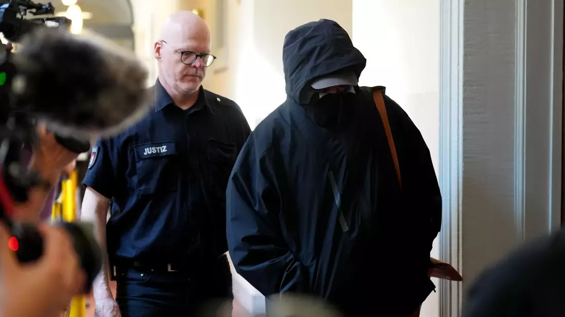 Ein Angeklagter wird von einem Polizisten zum Gerichtssaal begleitet.  - Bild: Marcus Brandt/dpa