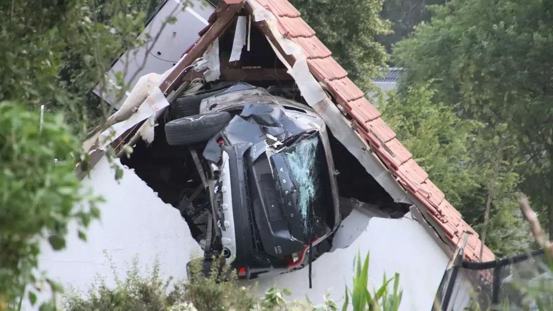 Das Auto liegt nach einem kurzen Flug seitlich in der Mauer einer Scheune. - Bild: -/Moonshine Media/dpa