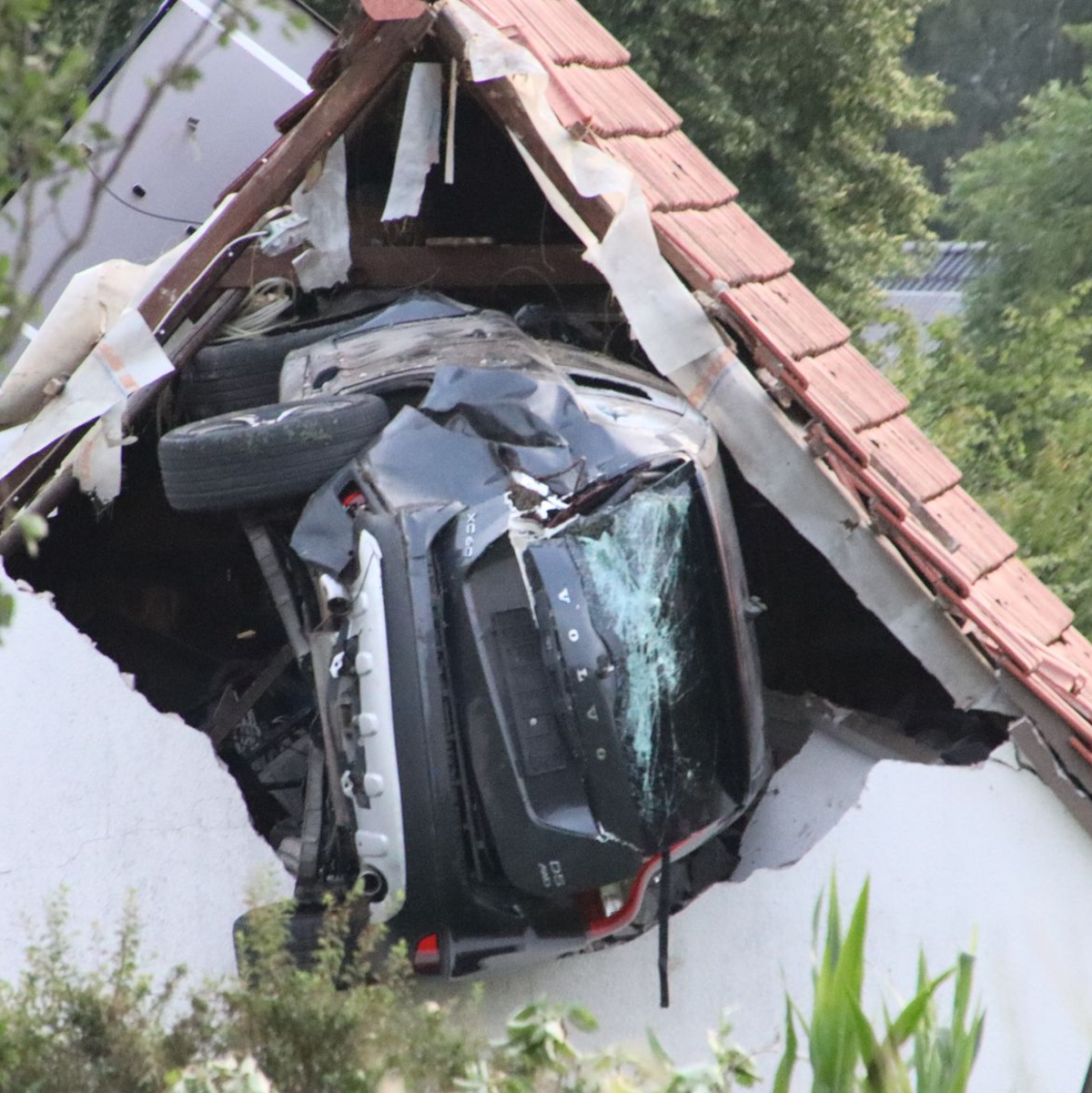 Das Auto liegt nach einem kurzen Flug seitlich in der Mauer einer Scheune. - Foto: -/Moonshine Media/dpa