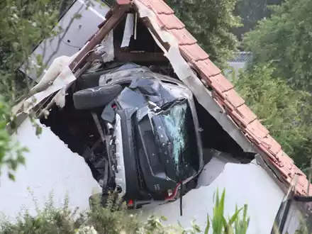 Das Auto liegt nach einem kurzen Flug seitlich in der Mauer einer Scheune. - Foto: -/Moonshine Media/dpa