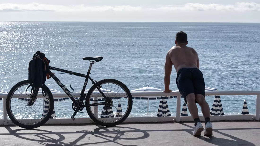 Ein Mann mit nacktem Oberkörper macht am Strand von Nizza neben seinem Fahrrad Übungen. (Archivbild) - Bild: Serge Haouzi/XinHua/dpa