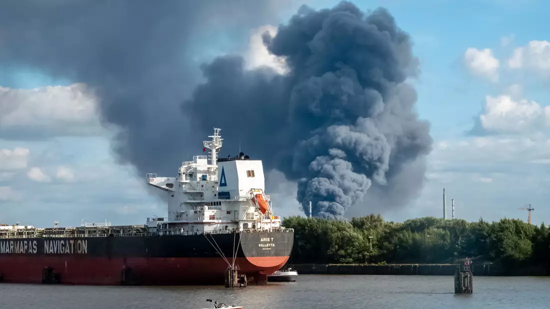 Rauch ist hinter einem Schiff zu sehen; in der Nähe des Einsatzortes fließt die Norderelbe.  - Bild: Bodo Marks/dpa