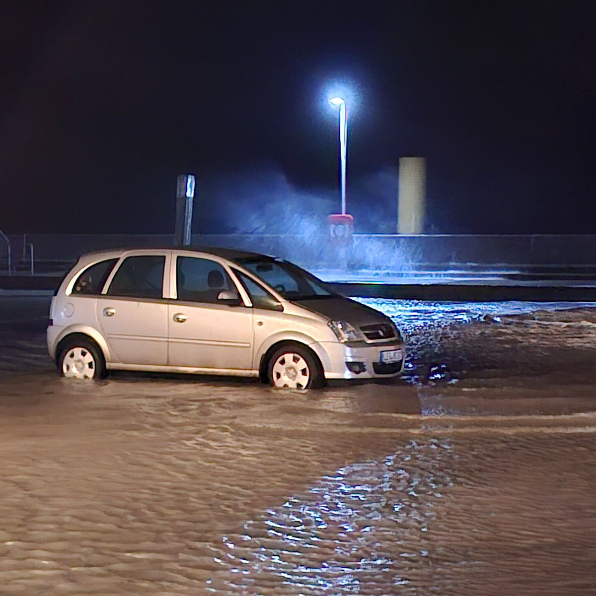 In Wilhelmshaven steht ein Auto auf einem überfluteten Parkplatz.  - Foto: Kai Moorschlatt/dpa