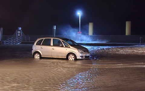 In Wilhelmshaven steht ein Auto auf einem überfluteten Parkplatz.  - Foto: Kai Moorschlatt/dpa