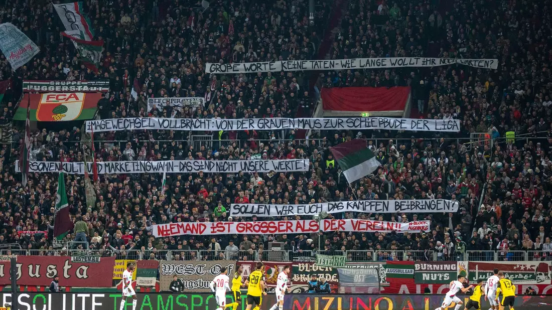 Die Augsburger Fans üben auf Spruchbändern Kritik am Weg der Vereinsführung mit Sandro Wagner. - Bild: David Inderlied/Kirchner-Media/dpa