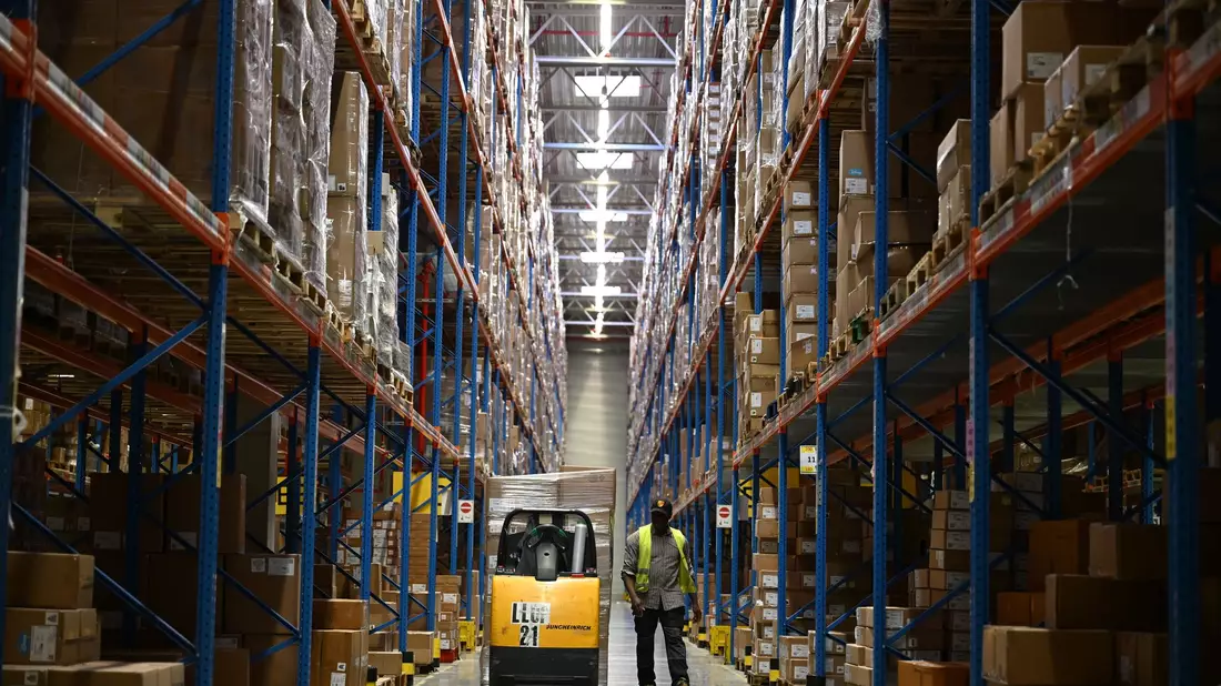 Ein DHL-Mitarbeiter nimmt Pakete in Emfpang - im Hintergrund ist ein Roboter zu sehen, der die Pakete aus einem Container nimmt und sie auf ein Förderband legt. (Archivbild) - Bild: Wolf von Dewitz/dpa