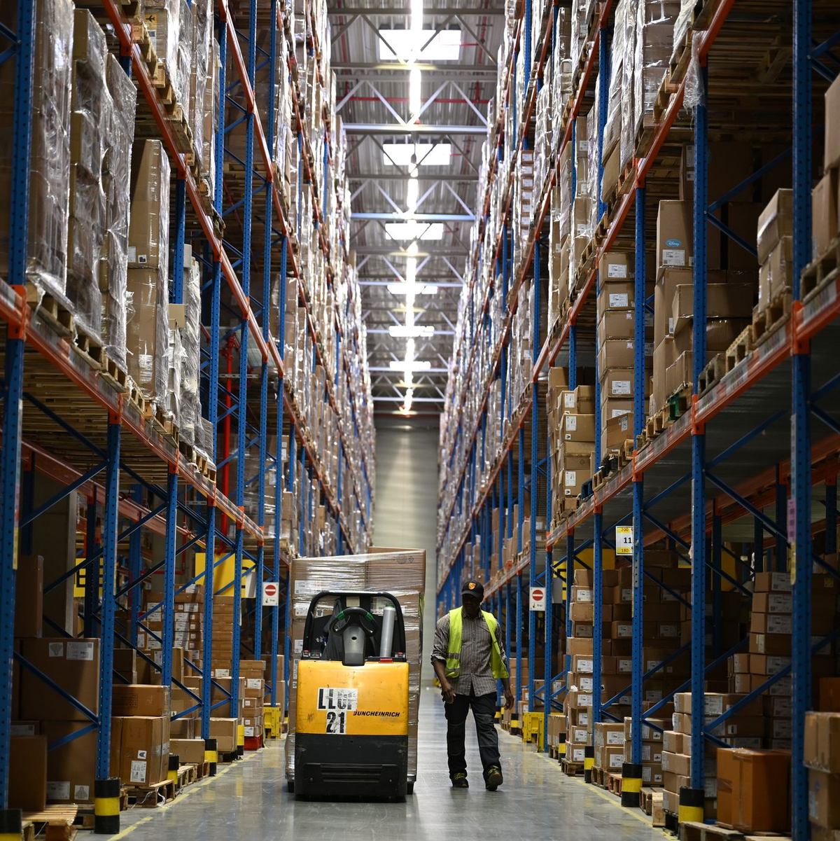 Ein DHL-Mitarbeiter nimmt Pakete in Emfpang - im Hintergrund ist ein Roboter zu sehen, der die Pakete aus einem Container nimmt und sie auf ein Förderband legt. (Archivbild) - Foto: Wolf von Dewitz/dpa