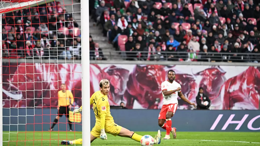 Bremens Torwart Mio Backhaus (l, Werder Bremen) und Ridle Baku (RB Leipzig) schauen dem Ball hinterher. Backhaus verhinderte mit seinen Paraden einen frühen Rückstand der Gäste in Leipzig. - Bild: Jennifer Brückner/dpa