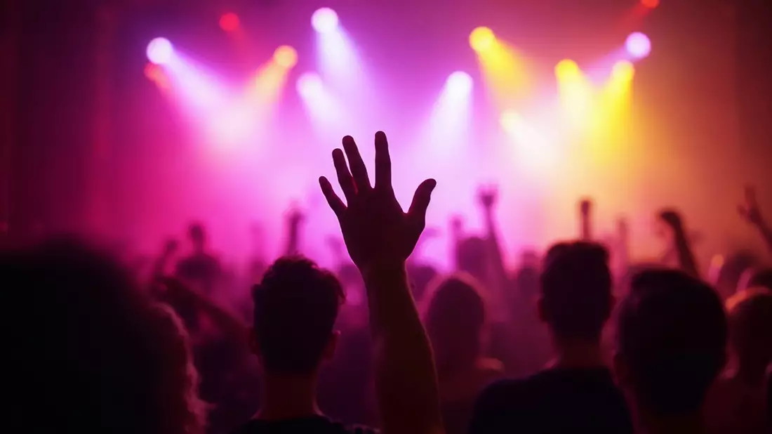 Erhobene Hand vor Publikum in pink-violettem Bühnenlicht beim Konzert
