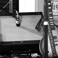 Stimmungsvolles Studiodetail in Schwarzweiß: Ein Mikrofon nimmt den Sound des Amps ab, daneben lehnt eine E-Gitarre mit Gurt. - Foto: THN