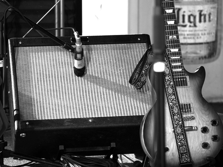 Stimmungsvolles Studiodetail in Schwarzweiß: Ein Mikrofon nimmt den Sound des Amps ab, daneben lehnt eine E-Gitarre mit Gurt. - Foto: THN