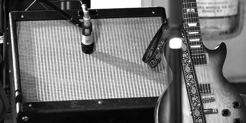 Stimmungsvolles Studiodetail in Schwarzweiß: Ein Mikrofon nimmt den Sound des Amps ab, daneben lehnt eine E-Gitarre mit Gurt. - Foto: THN