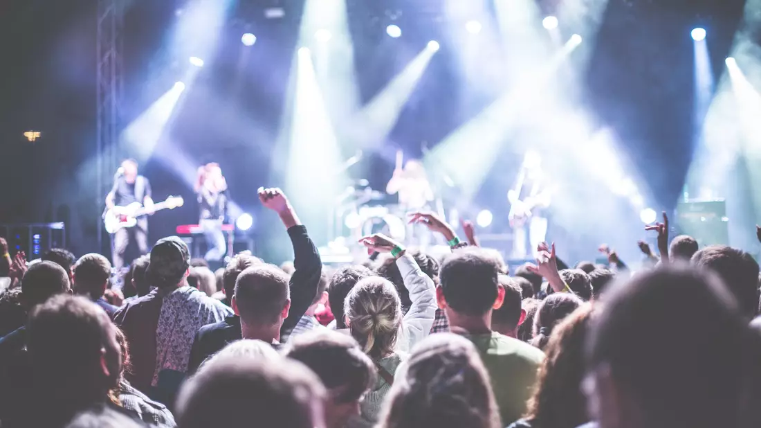 Publikum von hinten vor Bühne mit Band und blau-weißem Scheinwerferlicht