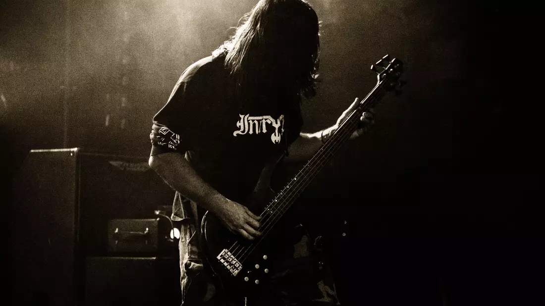 Langhaariger Bassist spielt im Gegenlicht auf einer Bühne in Sepia-Tönen