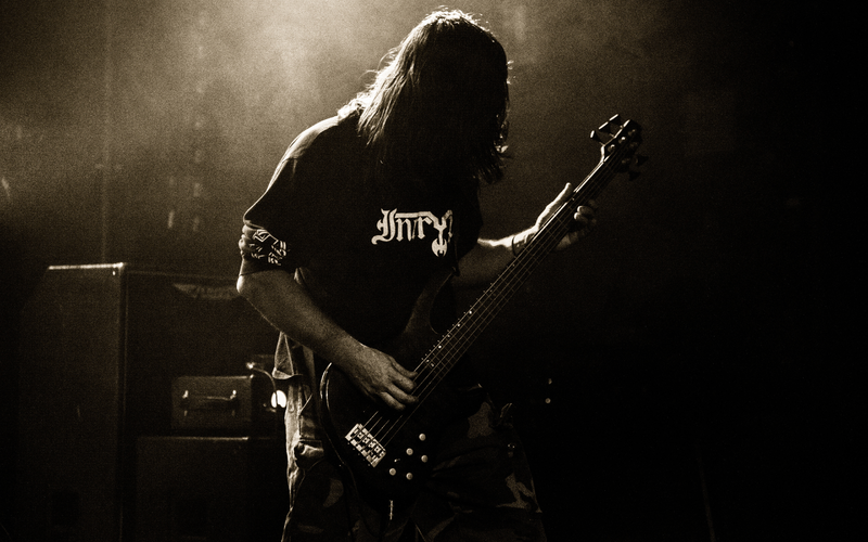 Voll im Rhythmus: Ein Bassist mit wehendem Haar verschmilzt im warmen Gegenlicht mit der rauen Atmosphäre der Bühne. - Foto: THN