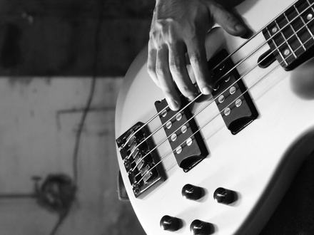 Fingerspitzengefühl im Detail: Die Hand des Musikers zupft die Saiten einer hellen Bassgitarre, festgehalten in Schwarzweiß. - Foto: THN