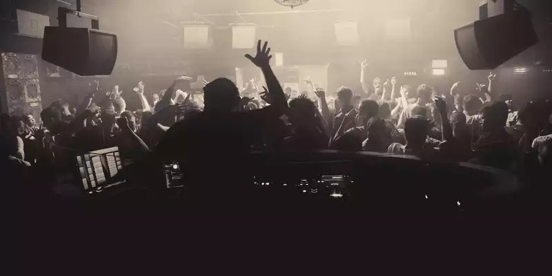 Partynacht im Club: Hinter dem Mischpult heizt der DJ der ausgelassenen Menge ein, während die Discokugel den Raum durchflutet. - Foto: THN