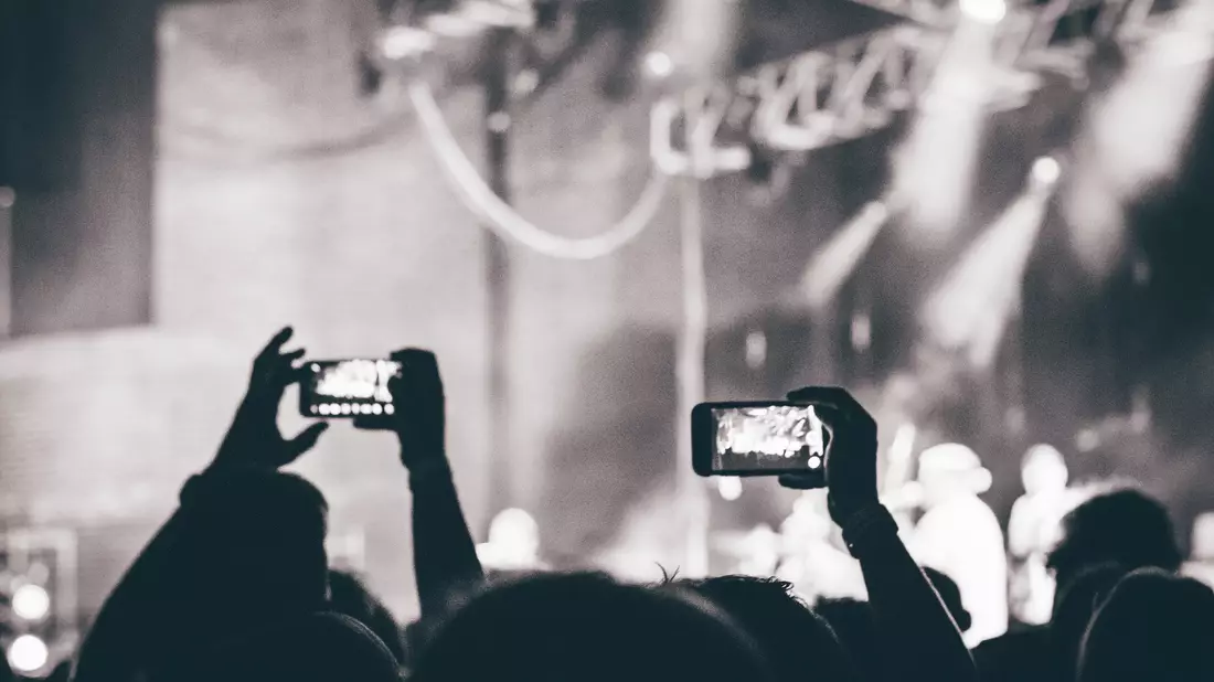 Zuschauer filmen Konzert mit erhobenen Smartphones vor der Bühne in Schwarzweiß