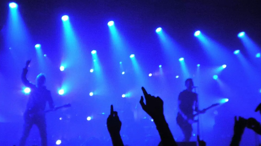 Band auf Bühne mit zahlreichen blauen Scheinwerfern und Publikumshänden davor