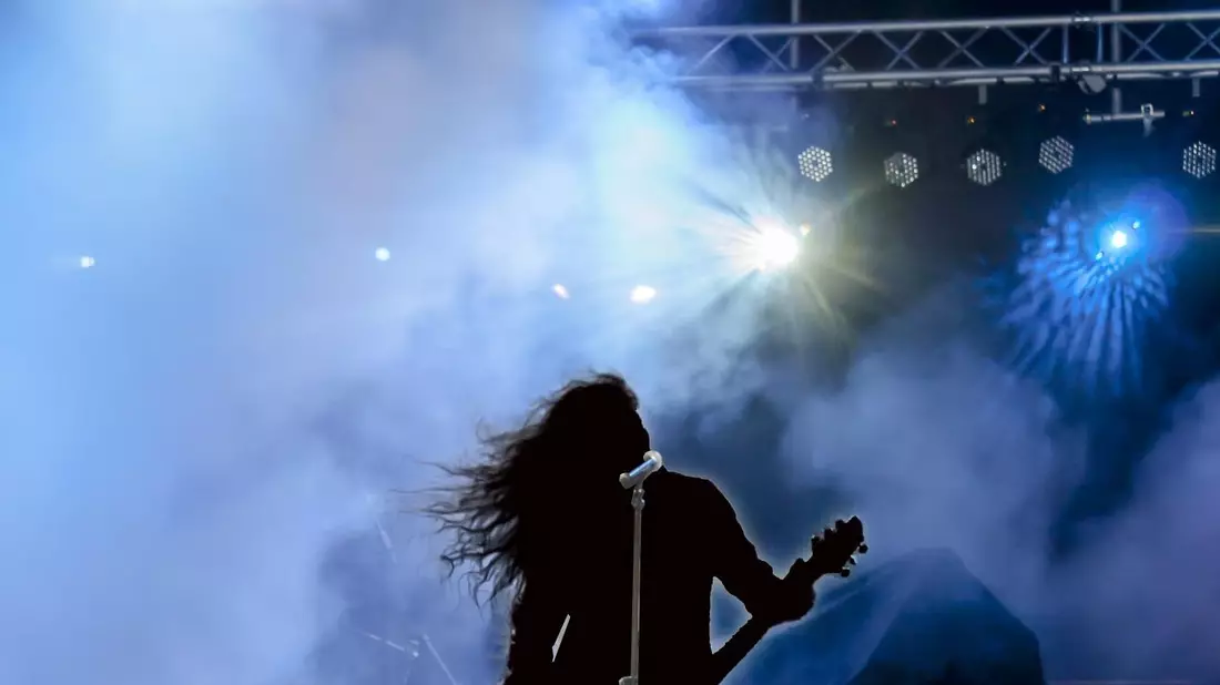 Gitarrist mit wehendem Haar als Silhouette im Bühnennebel und blauem Scheinwerf