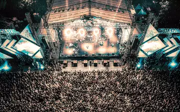Gigantische Dimensionen: Aus der Luft zeigt sich die volle Wucht des Festivals – eine endlose Menge vor der hell erleuchteten Bühne. - Foto: THN