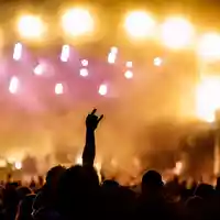 Symbol der Begeisterung: Eine Hand formt die Rockgeste vor einem Meer aus goldgelben und pinken Lichtern der Festivalbühne. - Foto: THN