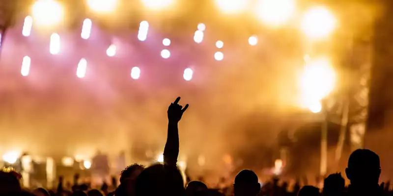 Symbol der Begeisterung: Eine Hand formt die Rockgeste vor einem Meer aus goldgelben und pinken Lichtern der Festivalbühne. - Foto: THN