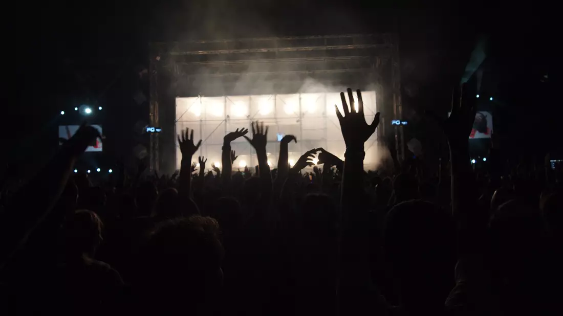 Erhobene Hände vor hell erleuchteter Festivalbühne mit Nebel im Nachthimmel