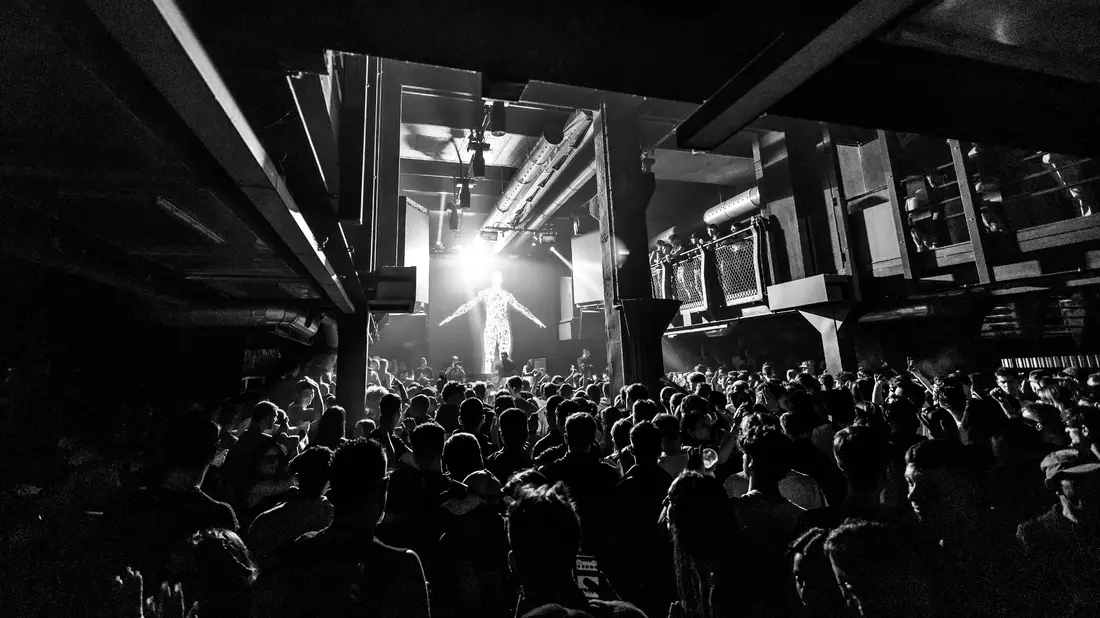 Sänger mit ausgebreiteten Armen im Gegenlicht vor Clubpublikum in Schwarzweiß