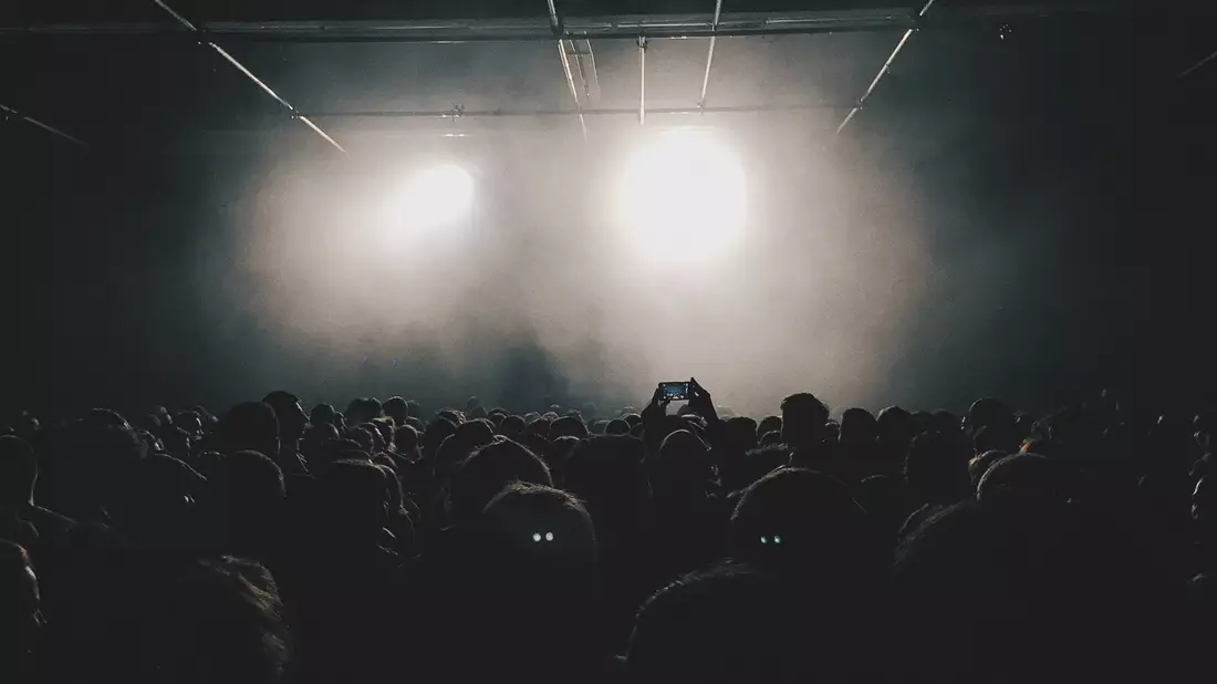 Dunkle Konzertmenge von hinten vor zwei hellen runden Spotlights und Bühnennebel