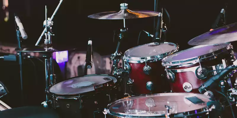 Bereit zum Anschlag: Ein rotes Drumset mit glänzenden Trommeln und Becken steht im gedämpften Licht startklar bereit. - Foto: THN