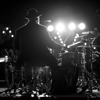Konzentration am Drumset: In Schwarzweiß sitzt der Schlagzeuger mit Hut vor einer Reihe gleißender Lichter und gibt den Takt. - Foto: THN