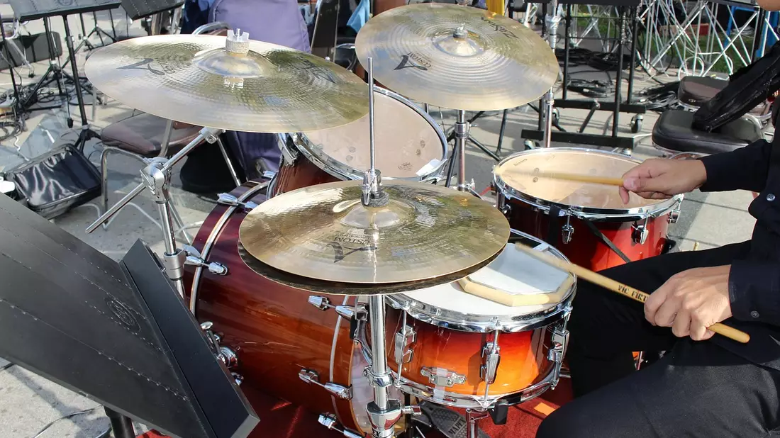 Schlagzeug mit goldbraunen Trommeln und Becken, Hand mit Drumsticks im Sonnenlicht