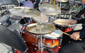 Mitten im Spiel: Die Hand des Drummers führt die Sticks über Snare und Becken des goldbraun schimmernden Sets im Freien. - Foto: THN
