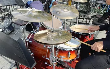 Mitten im Spiel: Die Hand des Drummers führt die Sticks über Snare und Becken des goldbraun schimmernden Sets im Freien. - Foto: THN