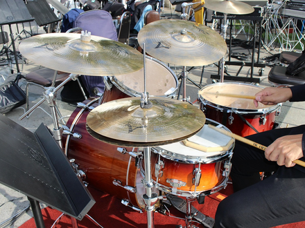 Mitten im Spiel: Die Hand des Drummers führt die Sticks über Snare und Becken des goldbraun schimmernden Sets im Freien. - Foto: THN