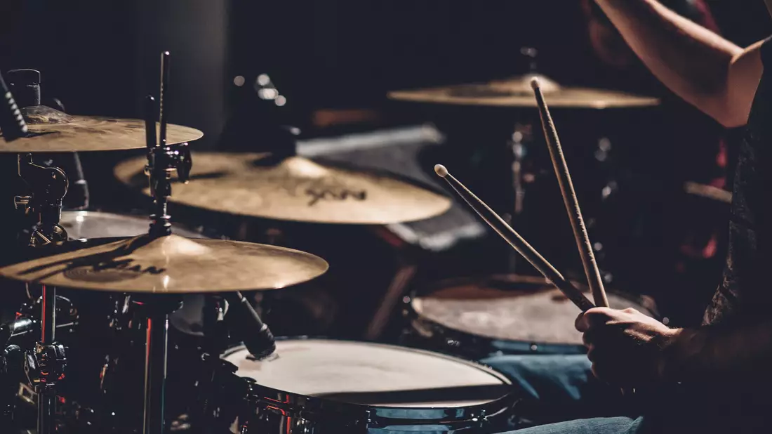 Schlagzeuger spielt mit Drumsticks an Becken und Snare in stimmungsvollem Licht