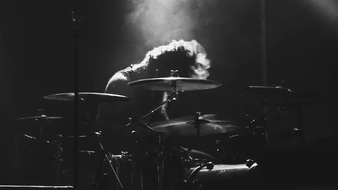 Schlagzeuger über sein Drumset gebeugt im hellen Spotlight als Schwarzweißfoto