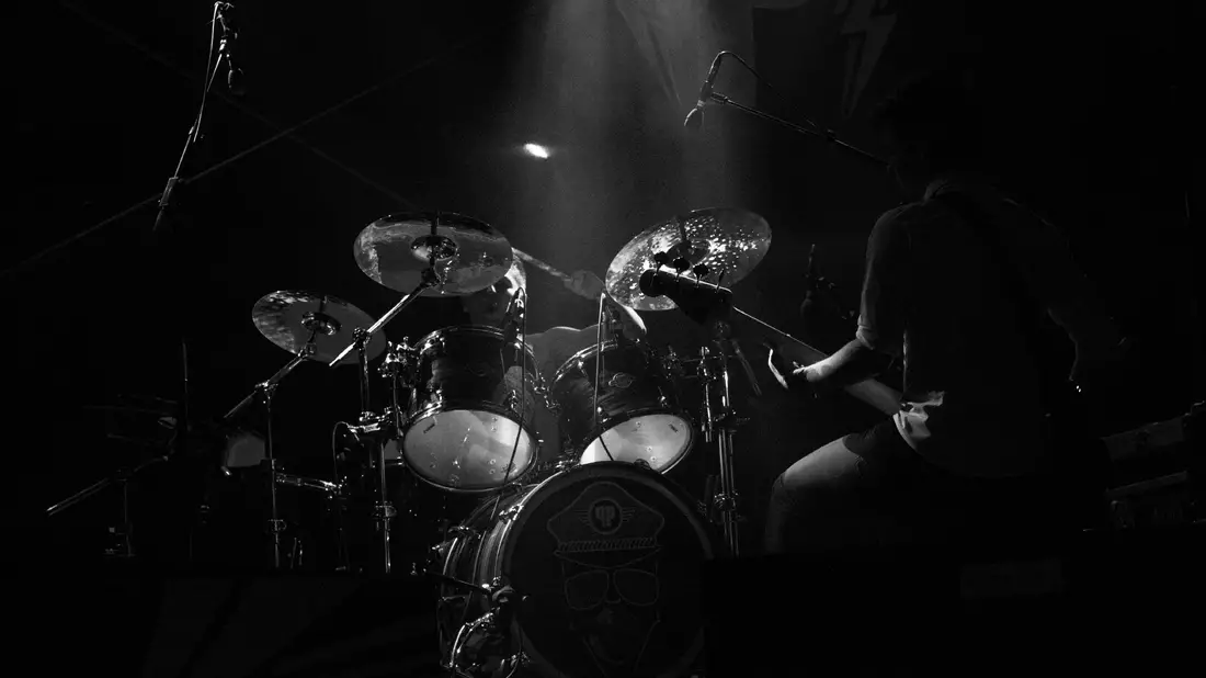 Schlagzeuger hinter großem Drumset auf dunkler Bühne mit Lichtstrahl in S/W