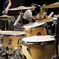 Zusammenspiel im Ensemble: Das helle Drumset rückt in den Fokus, während dahinter ein Saxofonist seinen Einsatz vorbereitet. - Foto: THN