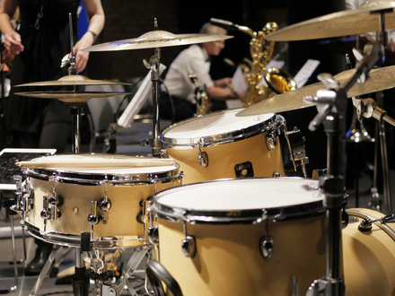 Zusammenspiel im Ensemble: Das helle Drumset rückt in den Fokus, während dahinter ein Saxofonist seinen Einsatz vorbereitet. - Foto: THN