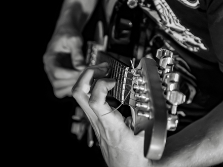 Präzision am Griffbrett: In Schwarzweiß greifen die Finger des Gitarristen einen Akkord, jede Saite klar im Fokus festgehalten. - Foto: THN