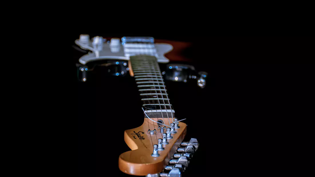 E-Gitarre mit Blick entlang des Halses zur Kopfplatte vor schwarzem Hintergrund