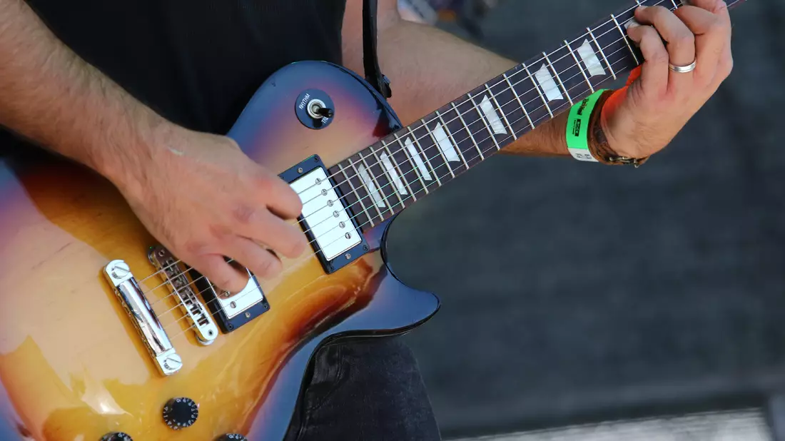 Musiker spielt Sunburst-E-Gitarre, Hände an Saiten und Griffbrett im Tageslicht