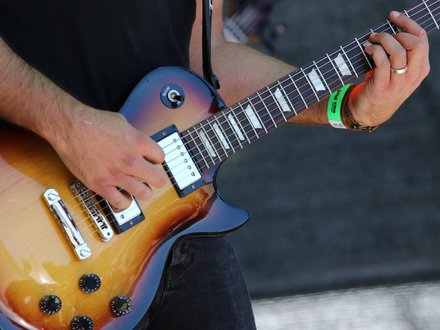 Im Spielfluss bei Tageslicht: Beide Hände des Gitarristen arbeiten an der Sunburst-Gitarre, Festivalbändchen inklusive. - Foto: THN