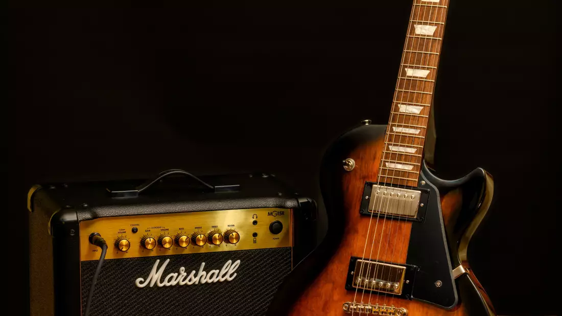 Sunburst-E-Gitarre neben kleinem Verstärker vor schwarzem Hintergrund im Studio
